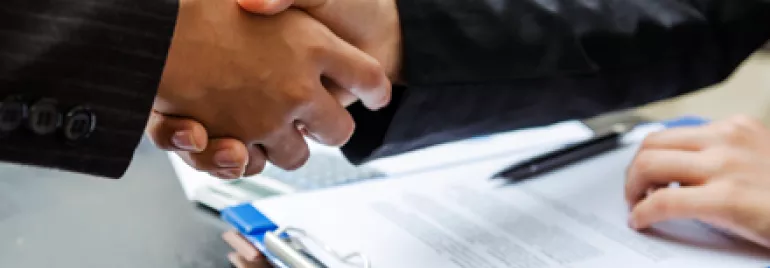 Dos personas se dan la mano frente a documentos.
