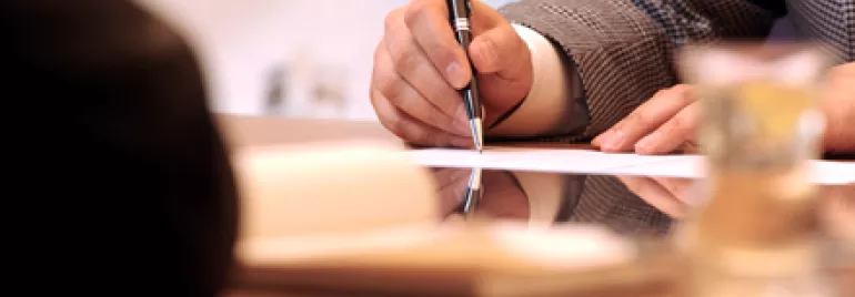 Persona firmando un documento en una reunión de negocios.