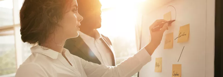 Dos personas discuten ideas en un pizarrón con luz de fondo.