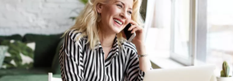 Mujer sonriendo mientras habla por teléfono en casa.