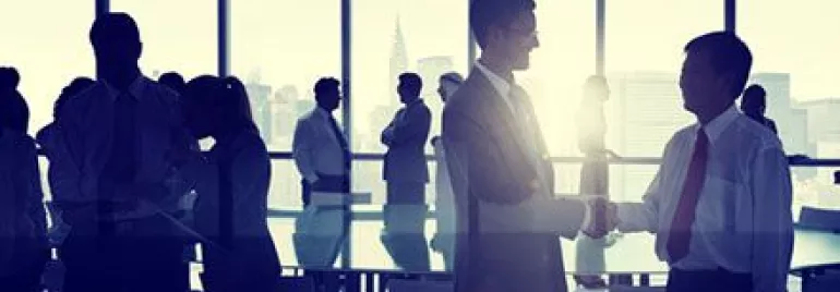 Personas de negocios estrechando manos frente a una ventana en una sala de reuniones.