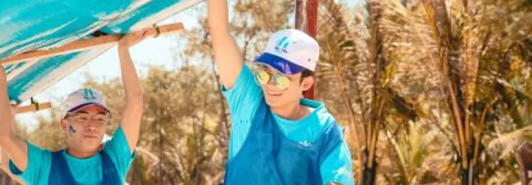 Dos personas con ropa azul cargan un inflable mientras sonríen bajo el sol.
