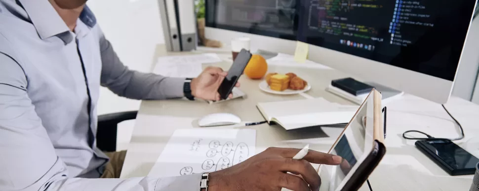Persona trabajando con una tableta y un ordenador en una oficina.