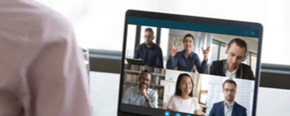 Persona participando en una videollamada con seis colegas en la pantalla de una laptop.