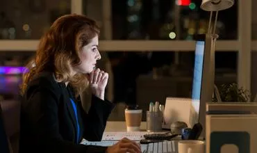 Mujer trabajando en la computadora por la noche, rodeada de papeles y una taza de café.