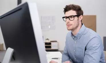 Hombre con gafas trabajando frente a una computadora.