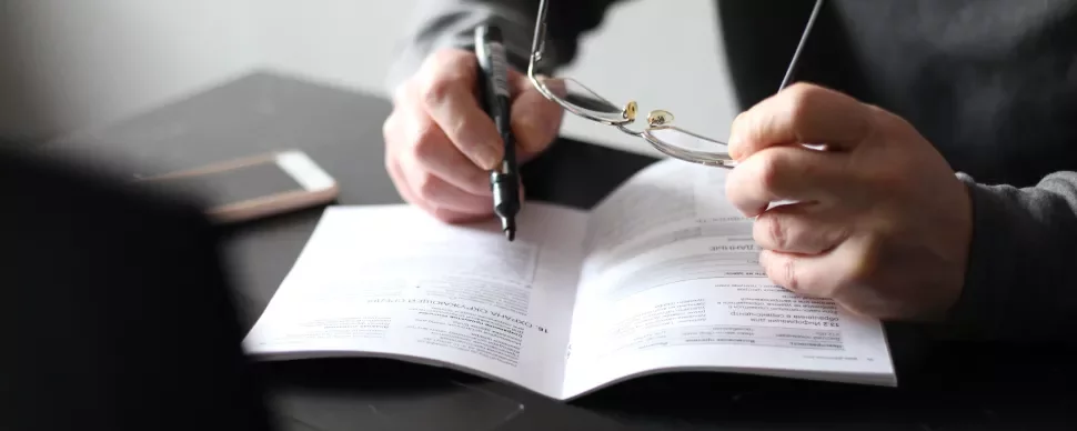 Persona leyendo un documento con gafas y bolígrafo en mano.