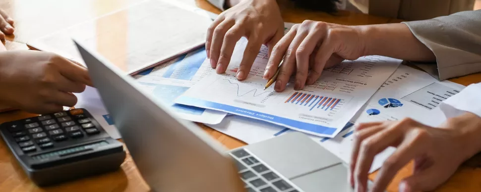 Manos revisando gráficos y documentos financieros en una reunión.