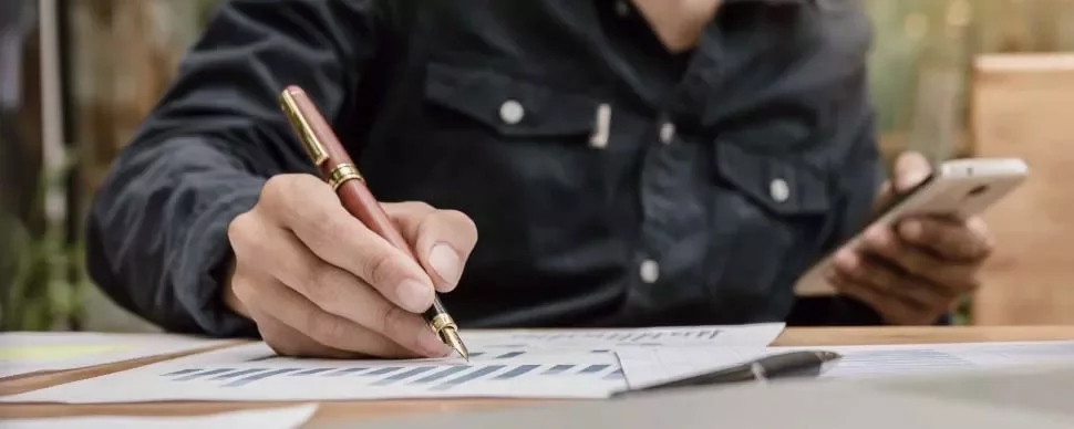 Persona revisando gráficos con un bolígrafo y un teléfono móvil.