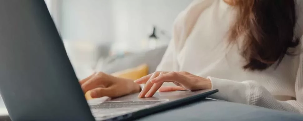 Mujer trabajando en una laptop en un sofá.