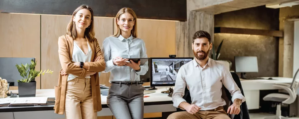 Tres personas en una oficina moderna, sonrientes y vestidas profesionalmente.