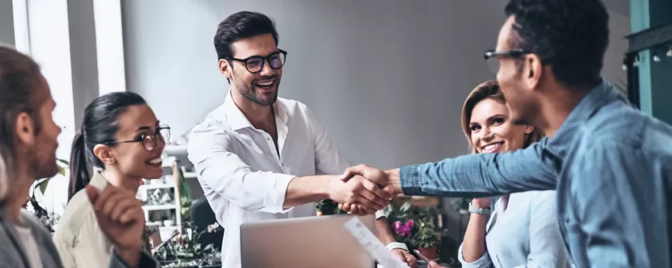Grupo de personas felices en una reunión, dos hombres dándose la mano.