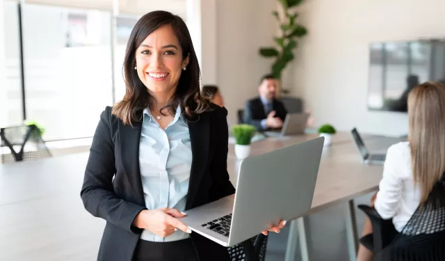 Mujer sonriente con portátil en oficina moderna.