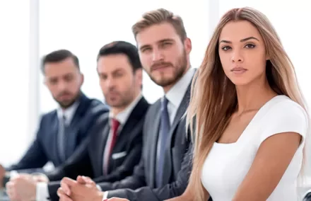 Grupo de personas en una reunión, vestidos de manera formal.