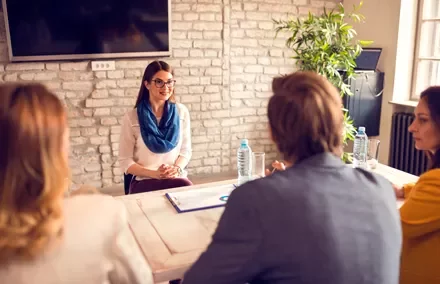 Mujer en entrevista de trabajo, sentada frente a tres personas en una oficina.