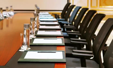 Mesa de conferencias con sillas y cuadernos alineados.