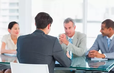 Reunión de negocios con cuatro personas en traje alrededor de una mesa.