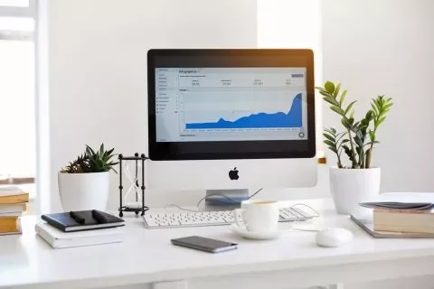Escritorio blanco con computadora, plantas y gráfica en pantalla.