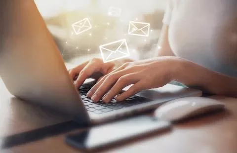 Persona usando una laptop con íconos de correo flotando.