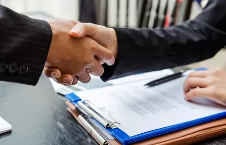 Dos personas se dan la mano frente a documentos.