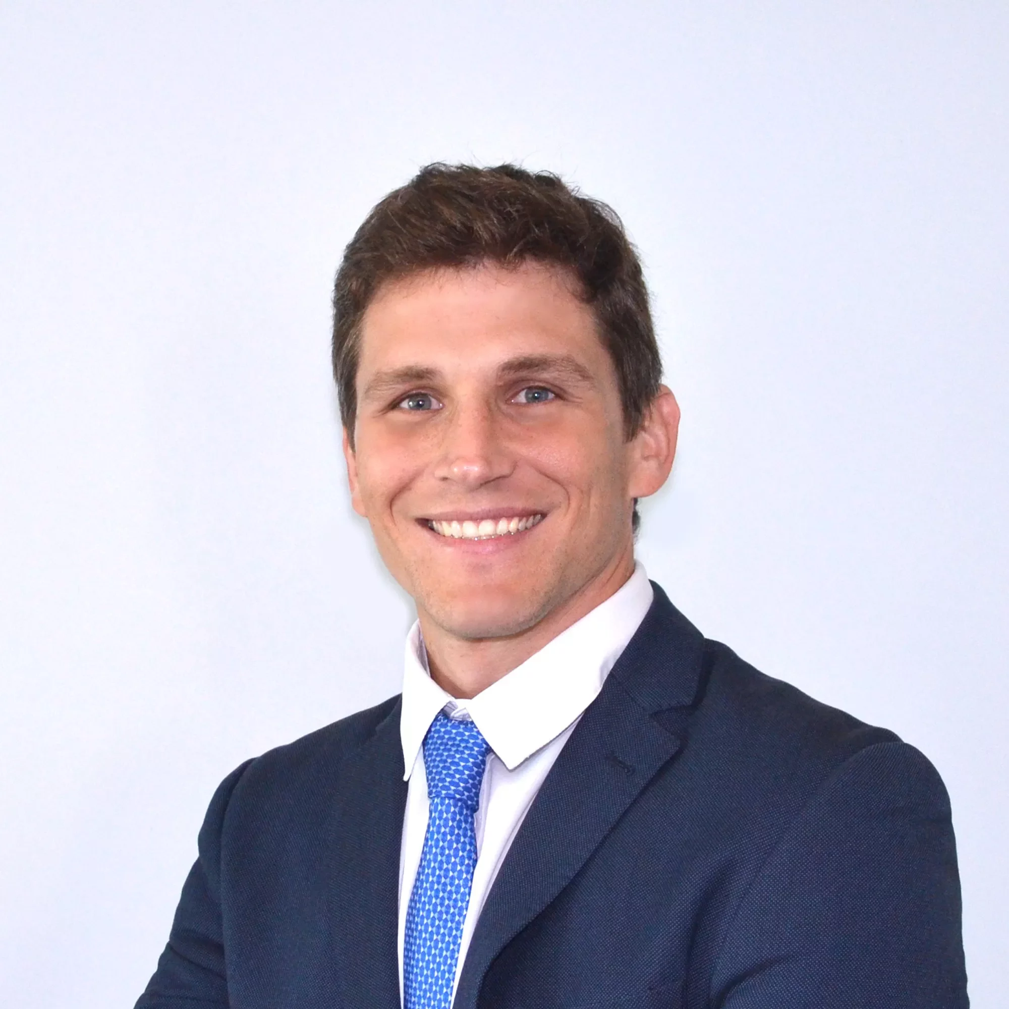 Persona en traje oscuro y corbata azul sonriendo al frente.