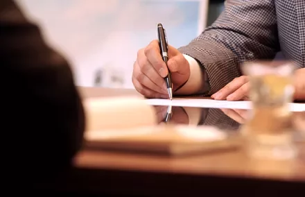 Persona firmando un documento en una reunión de negocios.